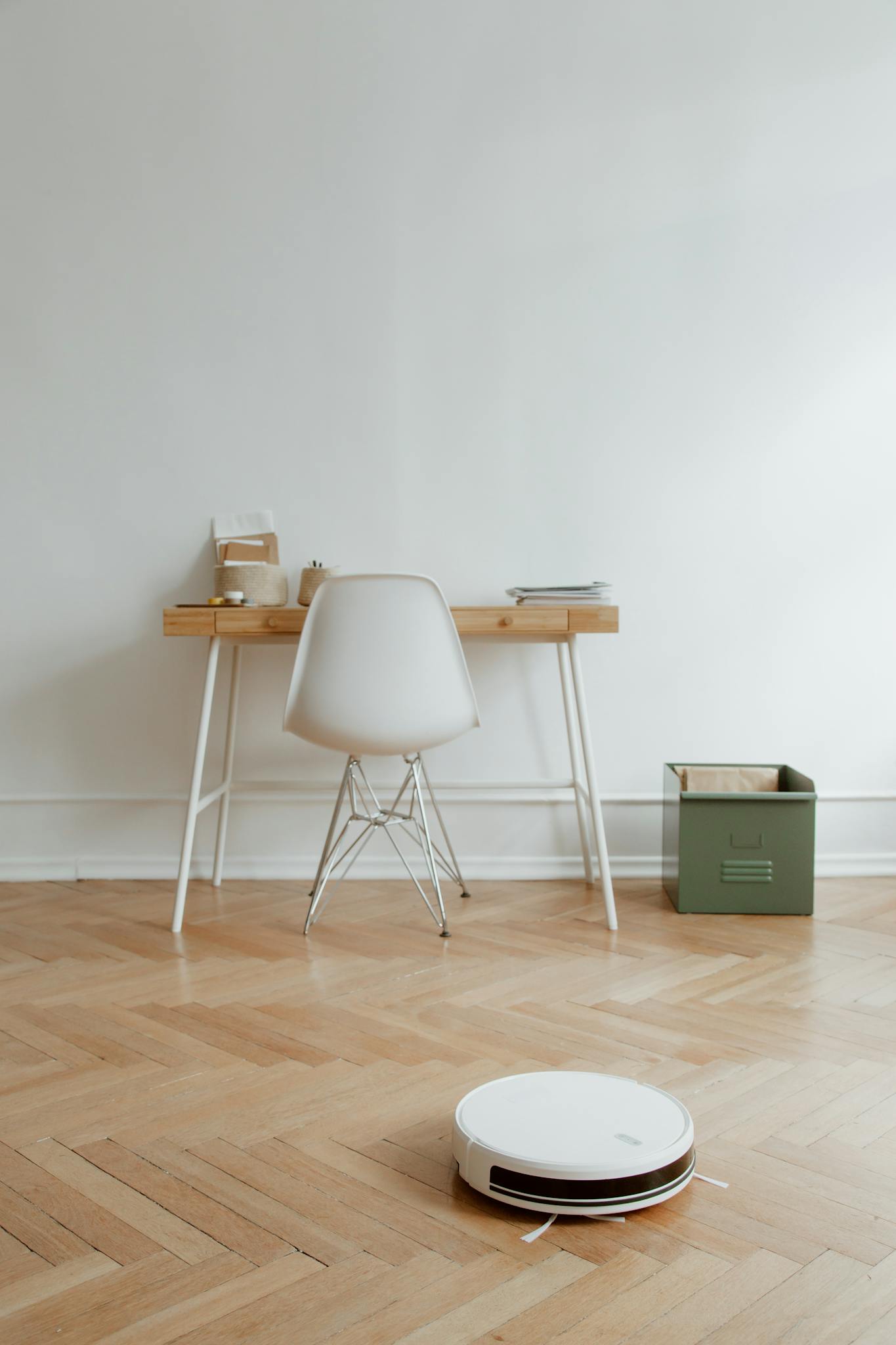 A sleek home office setup with a robot vacuum cleaning the wooden floor, emphasizing minimalism.